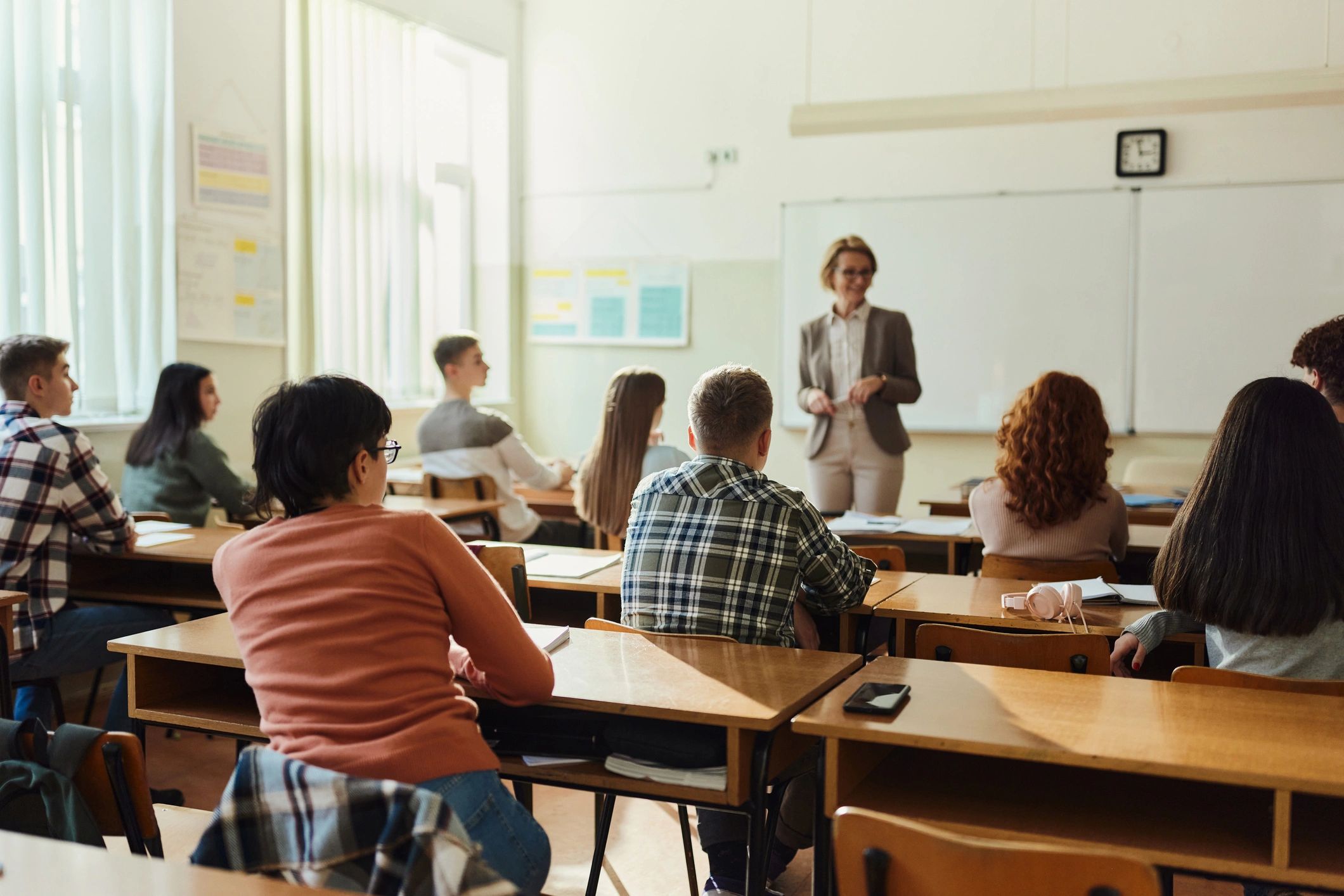 Rear view of large group of students listening to their high school teacher on a class in the classroom.